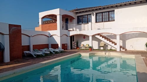 Área de piscina de Masia Rural Ca l'Eloi Janet con agua turquesa, tumbonas blancas y arquitectura mediterránea en Barcelona