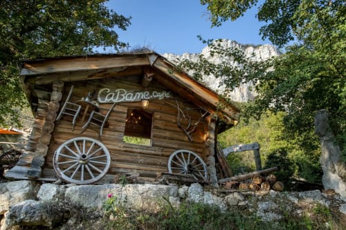 Rustic wooden cabin with wagon wheels at Maison de Sophie, a charming B&B nestled in Rencurel, France with mountain backdrop