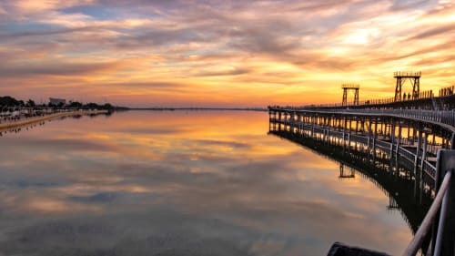 Atardecer en el muelle de Huelva con cielo dorado reflejado en aguas tranquilas y estructura de madera del embarcadero