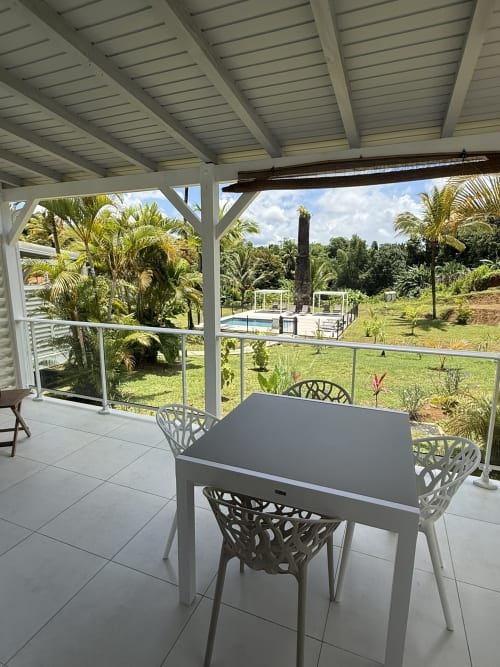 Terrasse couverte du Domaine de la Glacière avec table de repas, jardins tropicaux et vue sur la piscine à Petit-Bourg