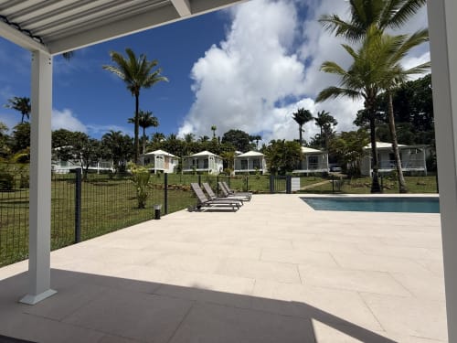 Espace détente au bord de la piscine du Domaine de la Glacière avec palmiers, bungalows et ciel bleu à Petit-Bourg, Guadeloupe