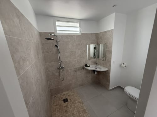 Modern bathroom at Domaine de la Glacière with walk-in shower, corner sink, toilet, and window in Petit Bourg