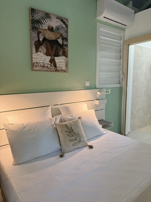 Modern bedroom at Domaine de la Glacière with mint green walls, white bedding, and tropical artwork in Petit Bourg