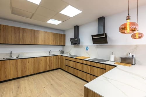 Modern kitchen at Residencia Demar hotel in Godella with wood cabinets, black countertops, and copper pendant lights