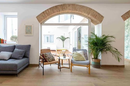 Sala de estar moderna en Residencia Demar, Godella con arco de ladrillo, sofá gris, muebles de madera y plantas en macetas