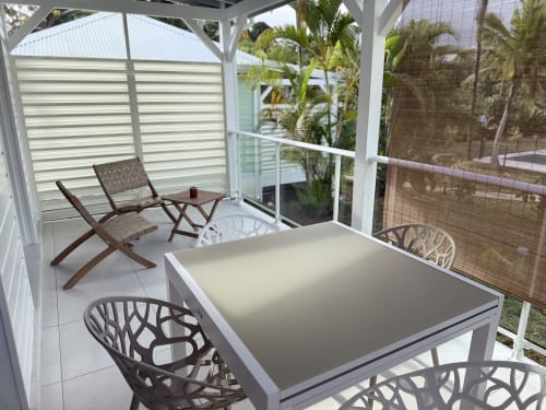 Patio couvert au Domaine de la Glacière avec table à manger, chaises longues et vue sur jardin tropical à Petit Bourg