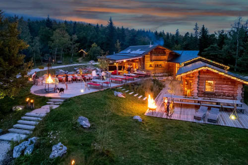 Maison de Sophie luxury lodge at dusk with illuminated log cabins, fire pits, and dining area in Rencurel forest