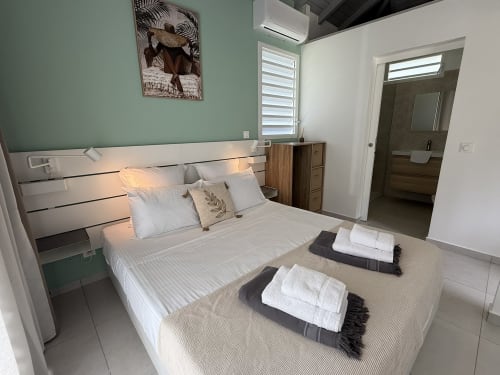Chambre moderne à la Domaine de la Glacière à Petit Bourg avec lit blanc, mur d'accent vert et salle de bain attenante.