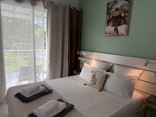 Chambre moderne au Domaine de la Glacière à Petit-Bourg avec lit queen-size, murs verts et accès au balcon