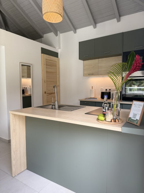Cuisine moderne du Domaine de la Glacière avec comptoirs en bois clair, armoires vert sauge et décoration de fleurs tropicales