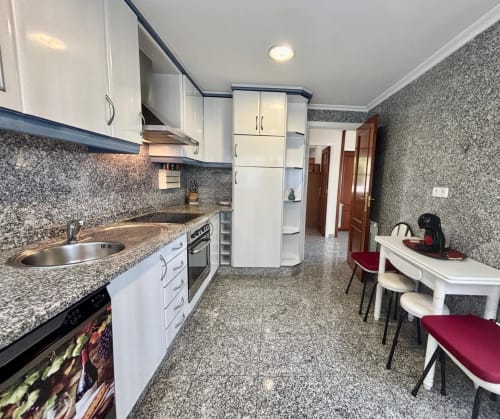 Cocina moderna de villa en Baiona con muebles blancos, encimeras de granito y comedor con sillas burdeos
