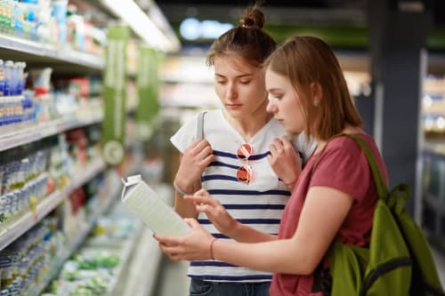 Due donne fanno shopping in un negozio di alimentari, esaminano le etichette dei prodotti vicino ai frigoriferi.