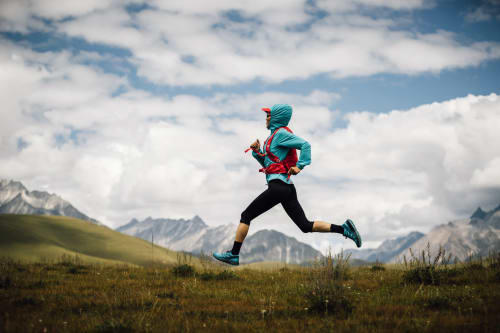 Trail runner in turquoise jacket jogging through mountain meadow near La Tour B&B in Oyace, Italy