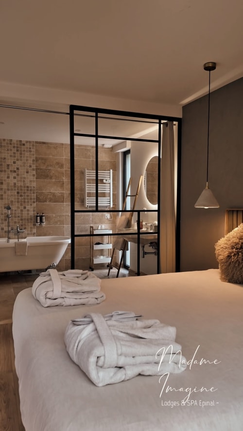 Lodge suite in Épinal with bed and bathrobes, open bathroom (freestanding tub, glass partition) and warm spa mood, wellness stay with private Nordic bath in the Vosges, Grand Est.