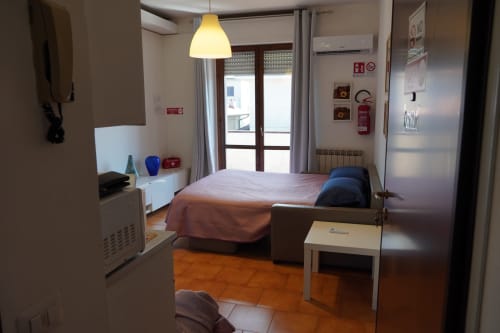 Carducci Apartment bedroom at THE V Collection in Turate with bed, pendant lamp, balcony doors, kitchenette, and terracotta