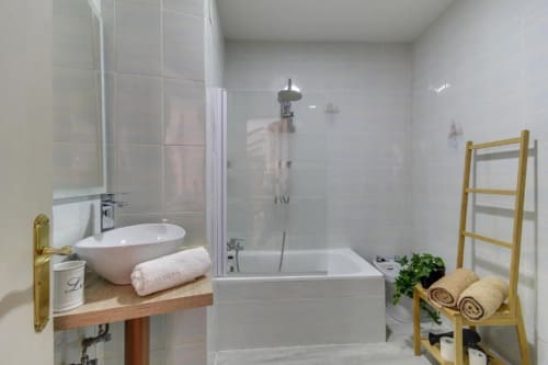 Baño moderno en villa de Salamanca con lavabo blanco, ducha efecto lluvia, toallero de madera y radiadores toalleros climatizados