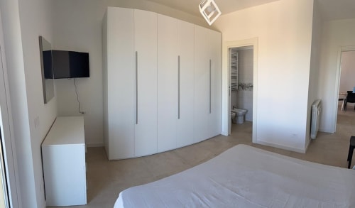 Camera da letto moderna in appartamento romano con letto, ampio guardaroba bianco, TV, bagno e arredamento minimalista