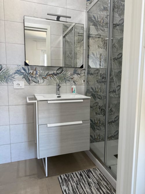 Bagno moderno in appartamento romano con piastrelle botaniche, vanità bianca, specchio e doccia walk-in