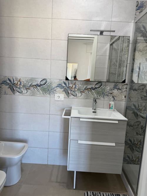 Bagno moderno in appartamento romano con lavabo bianco, specchio, bordo piastrellato decorativo, box doccia e wc