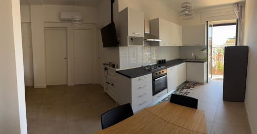 Cucina e zona pranzo moderna in appartamento romano con armadi bianchi, piano in nero, fornello, frigorifero e legno