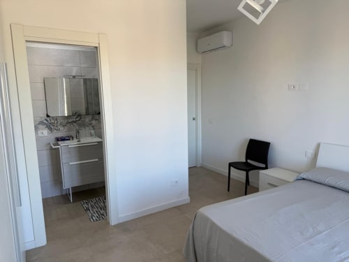 Camera da letto moderna con bagno ensuite, letto, sedia nera, aria condizionata e arredi contemporanei