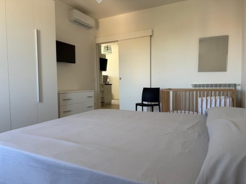 Camera da letto moderna a Roma con letto matrimoniale, lettino in legno, TV e bagno interno