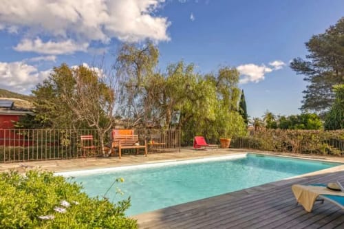 Piscine de la Villa Odette à Centuri avec eau turquoise, terrasse bois, transats et jardins méditerranéens luxuriants sous ciel bleu