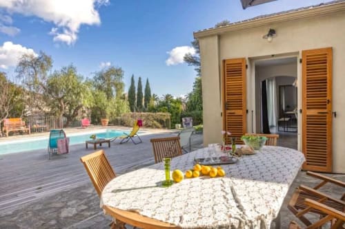 Terrasse piscine de la Villa Odette avec table à manger, chaises en bois, cyprès et jardin méditerranéen à Centuri, Corse