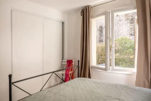 Chambre lumineuse à la Villa Odette à Centuri avec lit, tête de lit métallique, penderie et vue sur le jardin par de grandes fenêtres