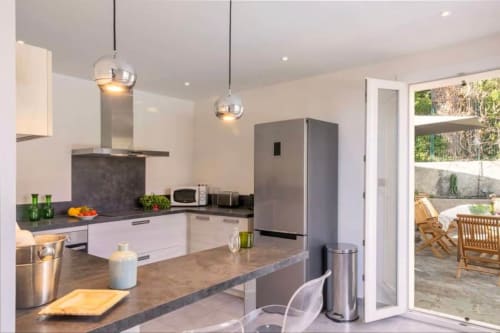 Cuisine contemporaine à la Villa Odette de La Conciergerie du Cap Corse à Centuri, avec mobilier blanc, plan de travail sombre et électroménager inox