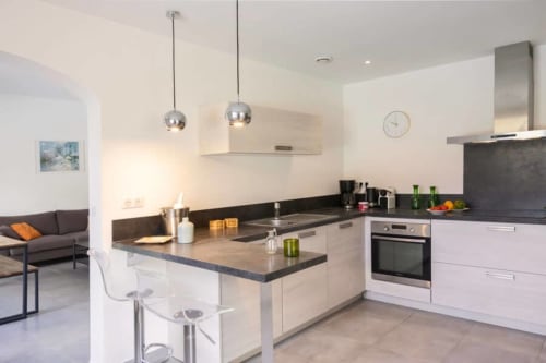 Cuisine moderne avec plan de travail noir, meubles blancs et îlot avec sièges à la Villa Odette, Centuri