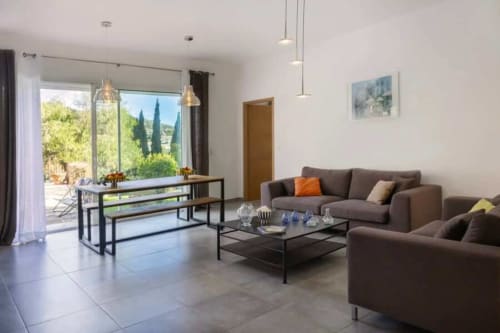 Salon moderne de la Villa Odette avec canapés marron, salle à manger et vue sur le jardin par les grandes fenêtres