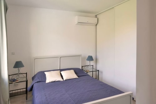 Chambre moderne de la Villa Odette avec literie bleue, tête de lit blanche, lampes de chevet, climatisation et décor épuré