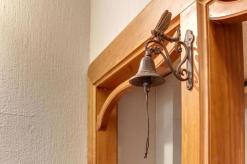 Campana de bronce ornamentada con detalle de libélula montada sobre la puerta de madera del hotel MoneoHeritage en Salamanca