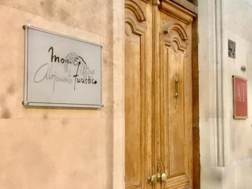 Letrero de pizarra con 'Moneo Alojamiento Turístico' frente a puerta de madera ornamentada en hotel de Salamanca, España