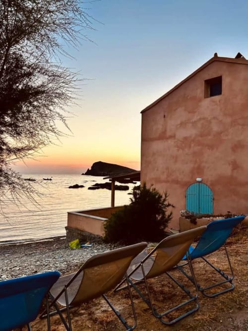 Vue coucher de soleil à la Villa Casapalmea à Centuri, Corse, avec transats et bâtiment en terre cuite surplombant la mer