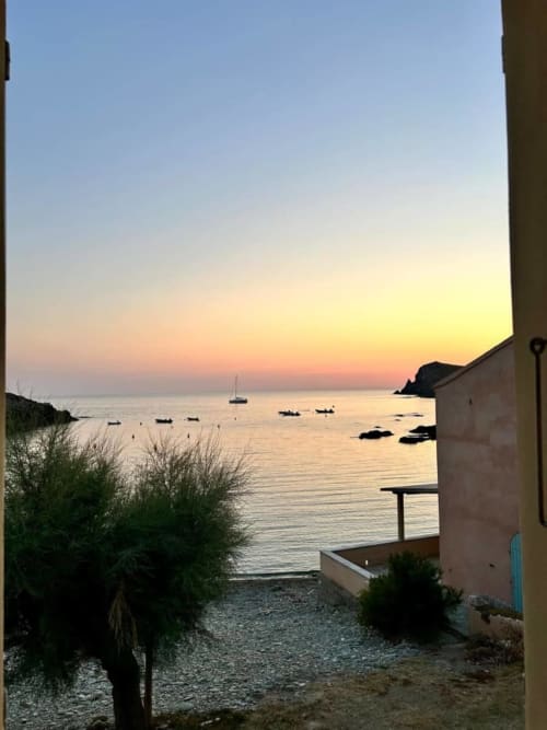 Vue au coucher de soleil sur le port de Centuri avec bateaux amarrés, végétation côtière et terrasse de villa à La Conciergerie du Cap Corse