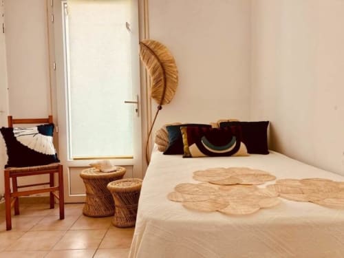 Chambre lumineuse à la Villa Casapalmea à Centuri avec accents tissés, chaise en bois, paniers décoratifs et porte donnant sur la mer