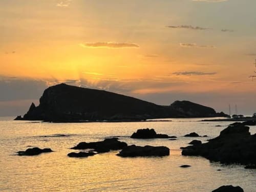Coucher de soleil doré sur une côte rocheuse avec silhouette d'île, vue mer depuis la Villa Casapalmea à Centuri, Corse