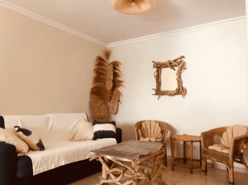 Salon de villa bohème avec fauteuils en rotin, canapé crème, table basse en bois flotté et décoration murale à Centuri, Corse