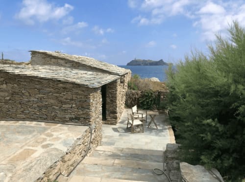 Terrasse de villa en pierre avec vue sur mer surplombant le port de Centuri, Corse, aménagée avec mobilier extérieur et jardin méditerranéen