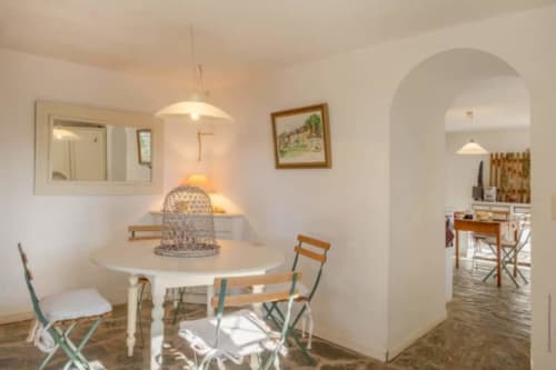 Salle à manger lumineuse à la Villa Cathy de La Conciergerie du Cap Corse avec table ronde, luminaire suspendu et entrée en arc.