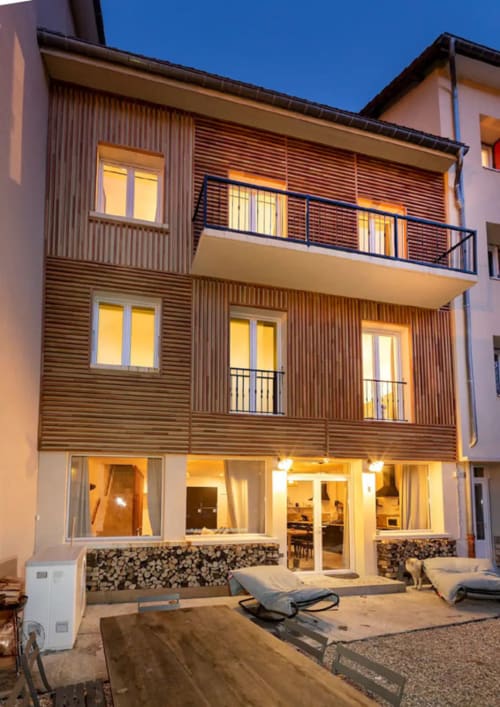 Maison de Sophie, cottage au crépuscule à Rencurel, façade en bois moderne avec fenêtres illuminées et terrasse de plain-pied