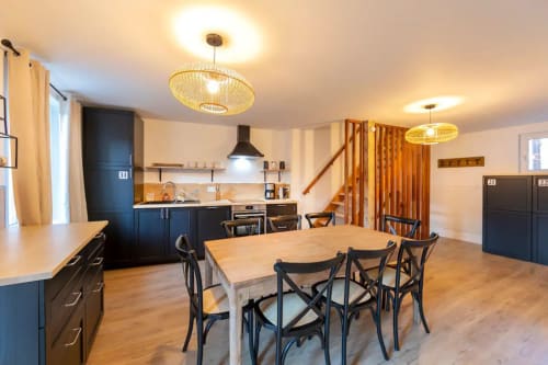 Open-plan kitchen and dining area in a Rencurel cottage with dark blue cabinetry, wooden table, and modern pendant lights