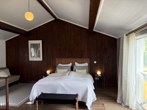 Spacious bedroom at Villa Várzea with dark wood walls, white bedding, pendant light, and patio access in Várzea