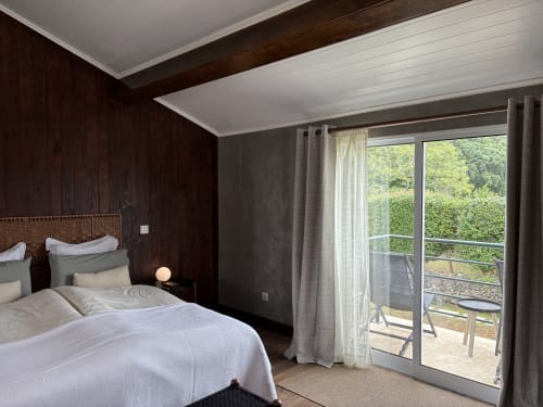 Modern bedroom at Villa Várzea with dark wood walls, white bedding, and glass doors opening to a mountain-view balcony in