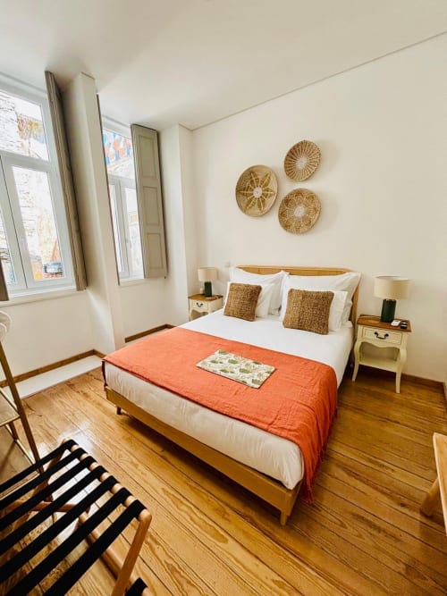 Bright double bedroom at Casa Tawny Pinhão with wooden bed, orange throw, woven wall art, and large windows