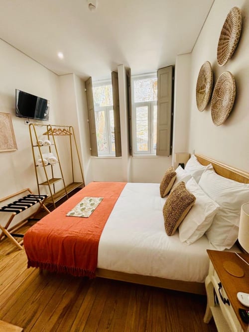 Cozy double bedroom at Casa Tawny in Pinhão with white bedding, orange runner, wooden furniture, and woven wall decor