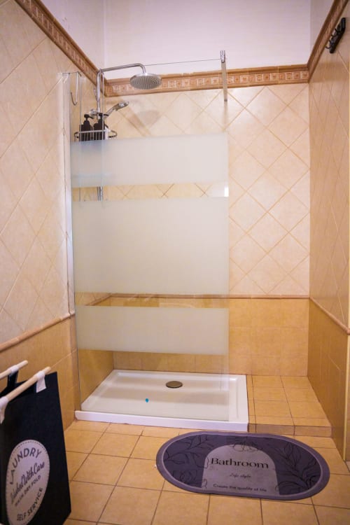 Modern bathroom with walk-in shower, white tile walls, golden ceramic floor, and bathroom mat at Navigli Affittacamere BnB in