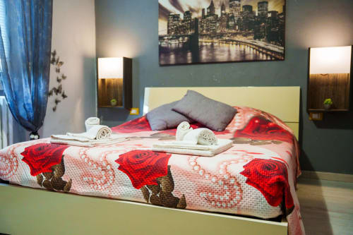 Modern bedroom at Navigli Affittacamere in Rozzano with red floral bedding, gray pillows, city skyline artwork, and